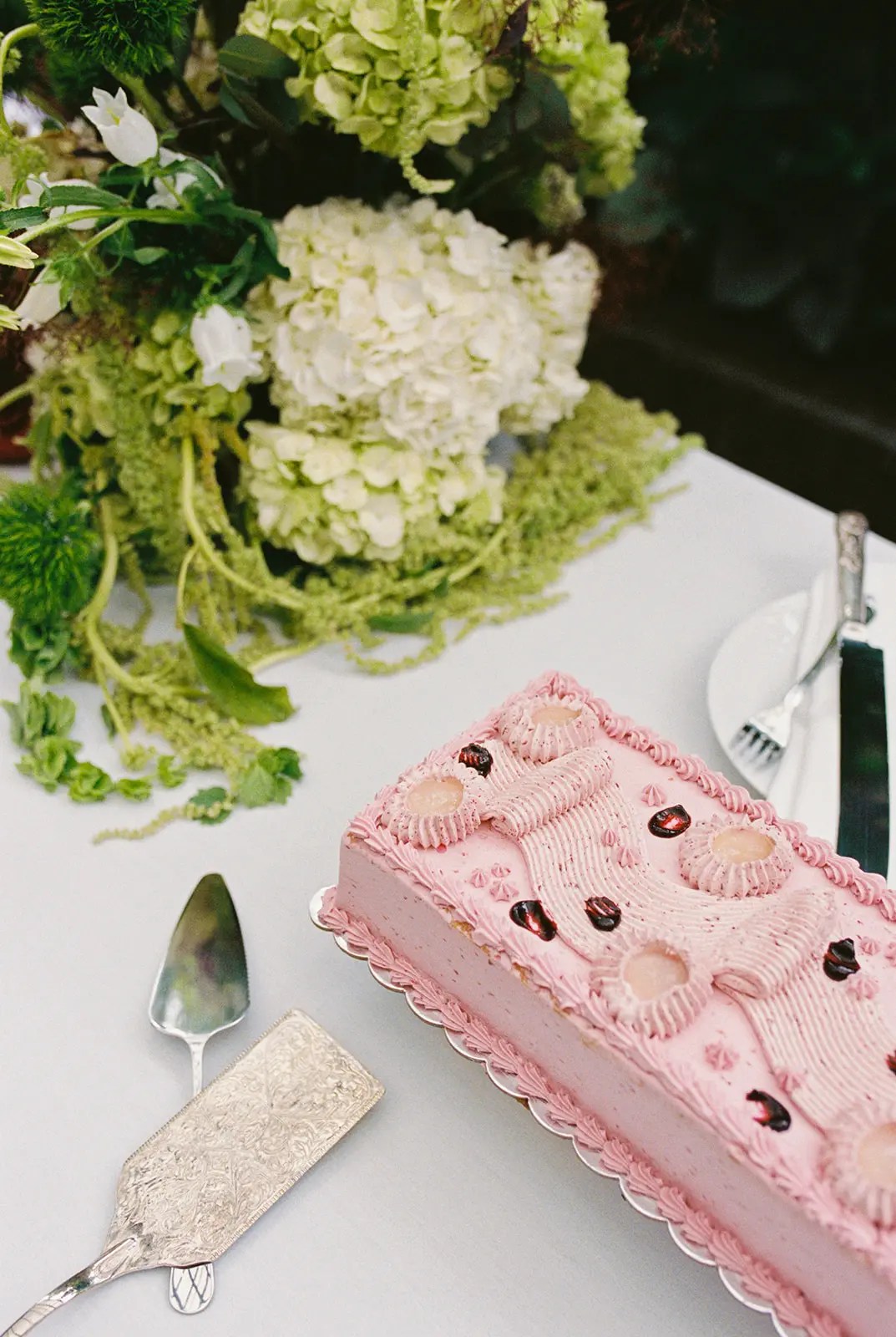 Gâteau en feuille de crème au beurre rose de Paper Cake Shop avec bordures en rosace passepoilées et garniture de fruits foncés brillants à côté d'une pelle à gâteau argentée