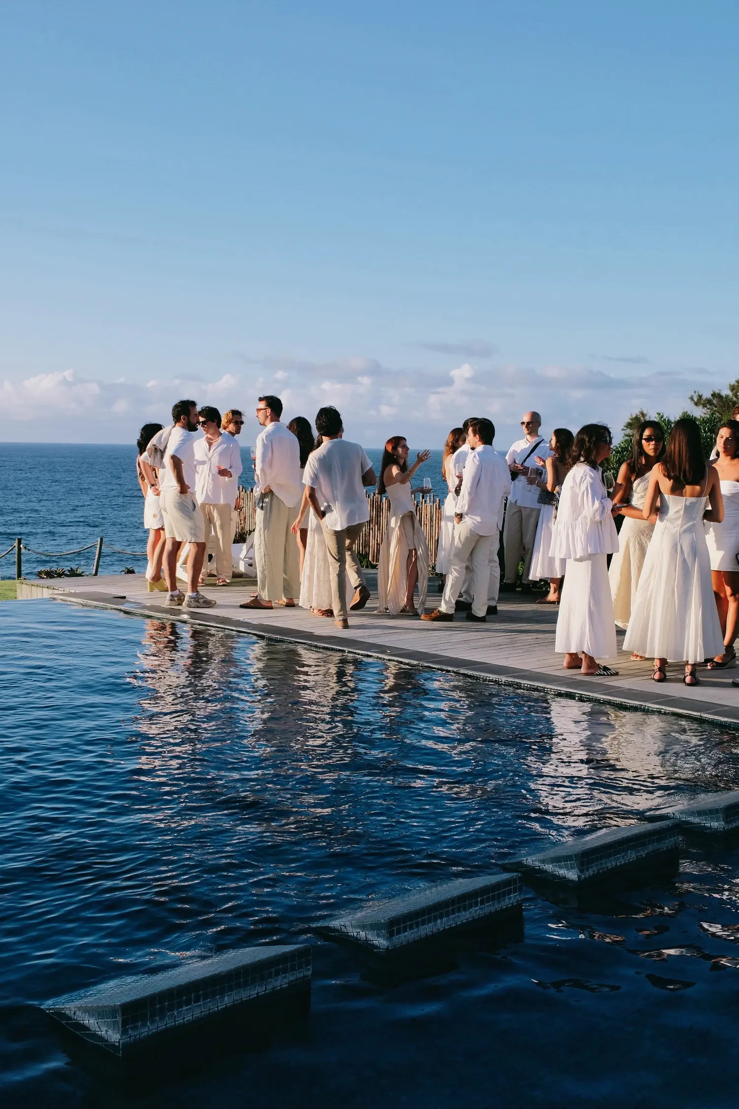 Wedding guests in an all-white dress code gathered on a pool deck above the ocean at Santa Barbara Eco Beach Resort, São Miguel