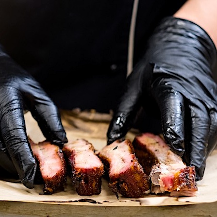 Grill restaurant kitchen. Cropped shot of chef in black cooking gloves serving smoked pork ribs.