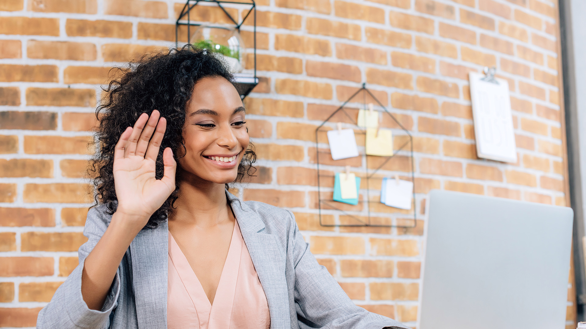 Grin Events San Diego | A business woman employing remote team building gestures in front of a brick wall.
