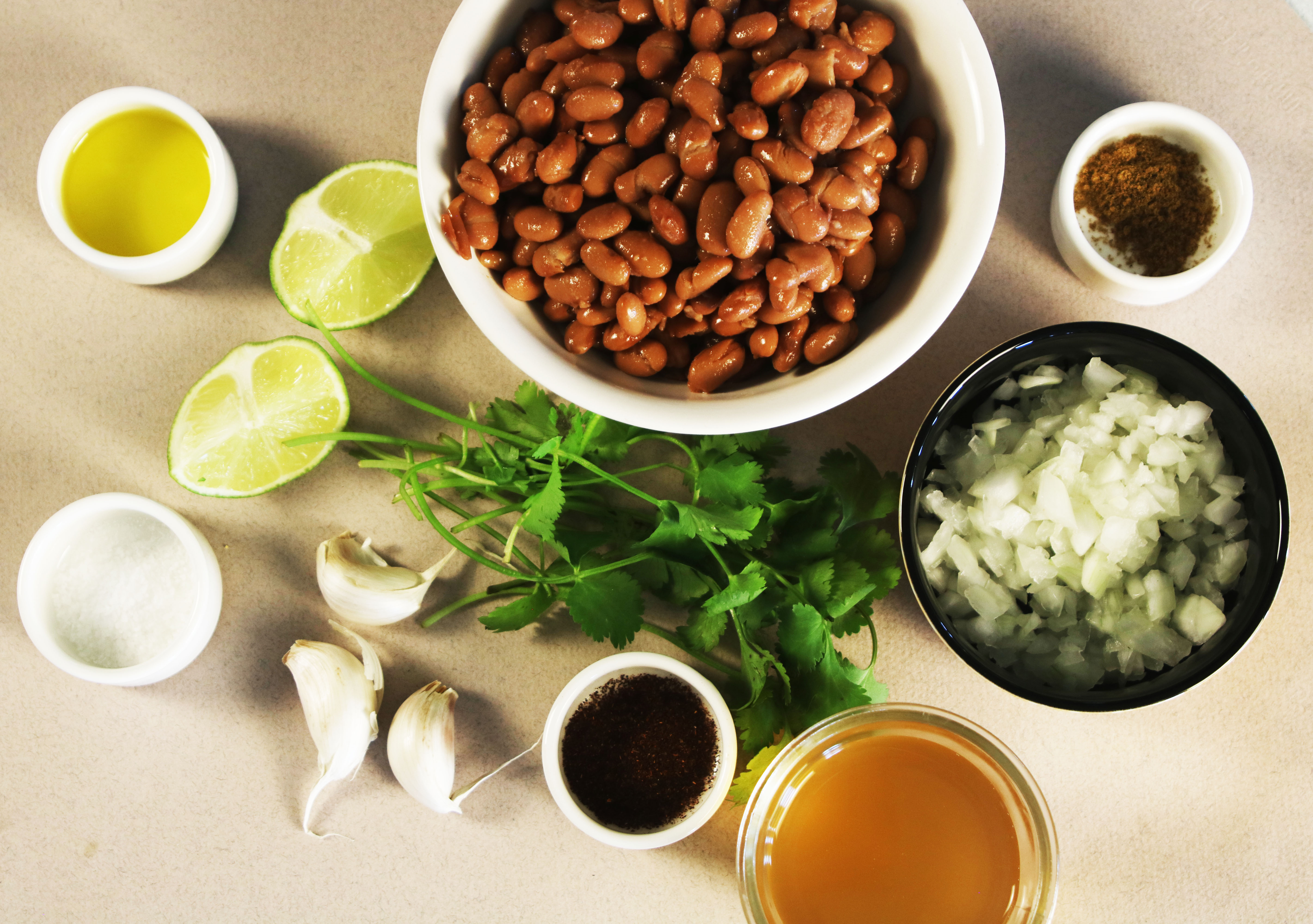 Ingredients for homemade classic refried beans including canned pinto beans, onion, garlic, olive oil, chicken broth, lime, cilantro, salt, cumin, and chili powder.