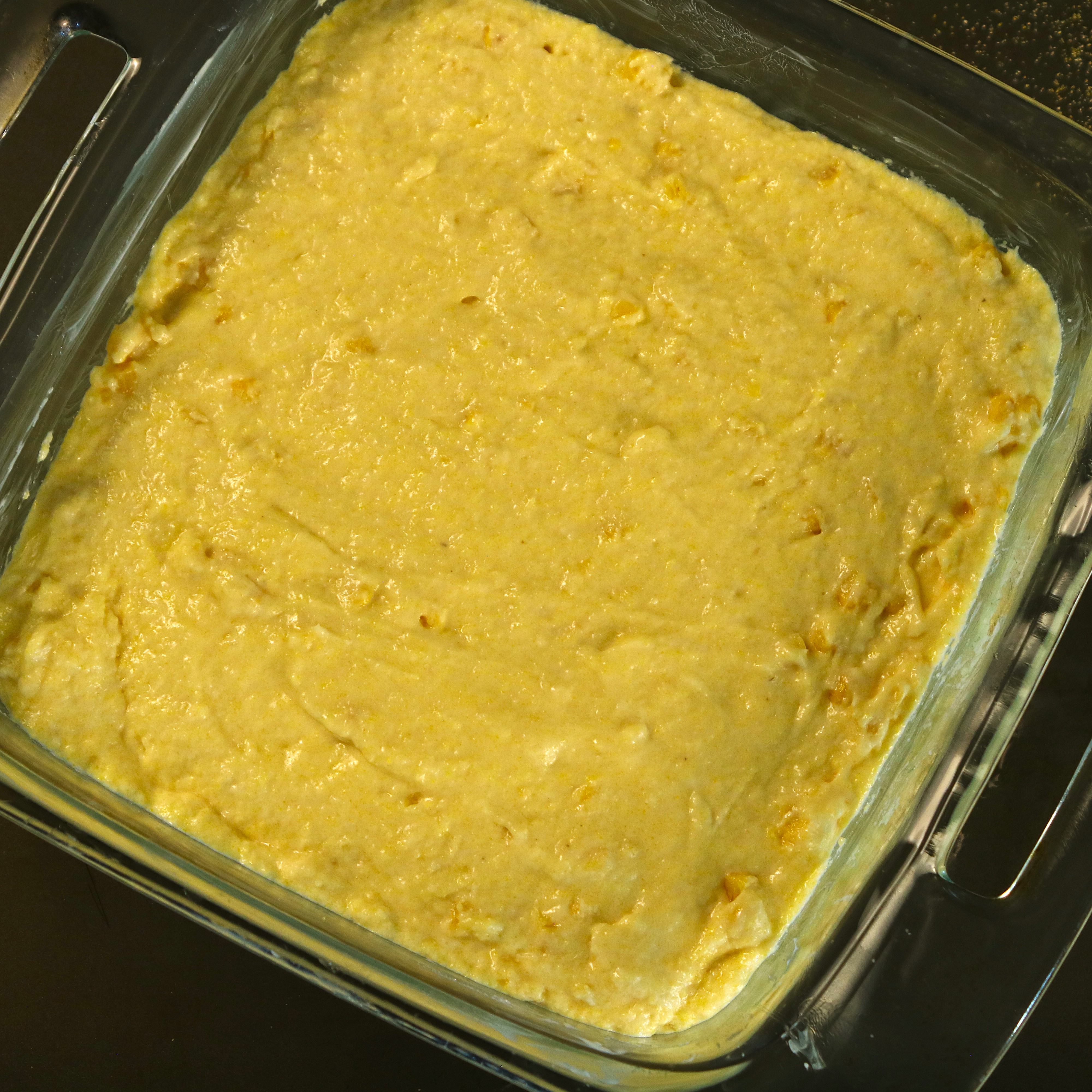 Unbaked cornbread batter spread evenly in a greased 8×8 glass baking dish, ready for the oven.