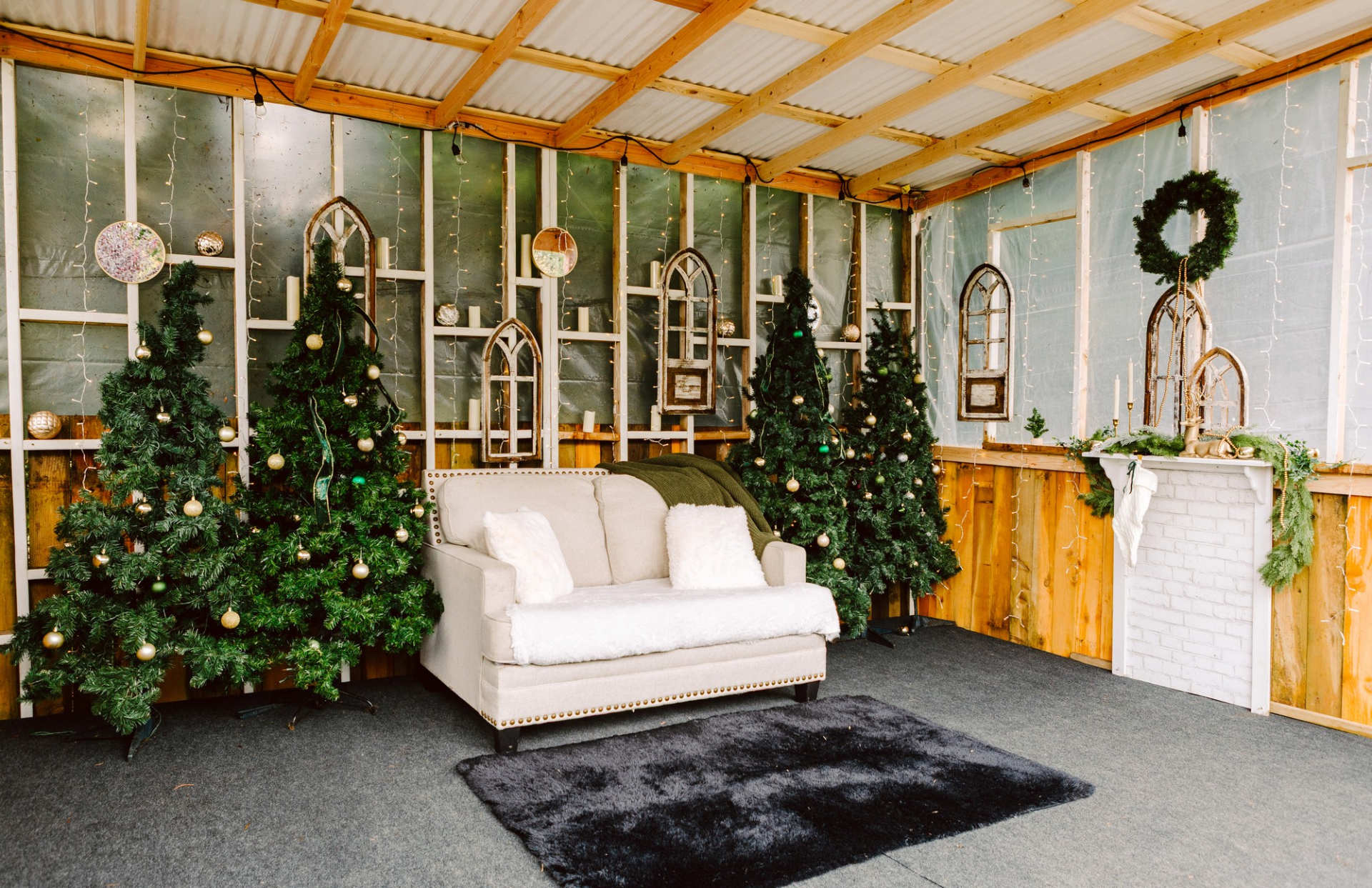 GSquared Weddings Photography A cozy indoor holiday scene with decorated Christmas trees, a white couch with pillows, a black rug, and a faux fireplace adorned with greenery and a wreath. The space features rustic wood and festive ornaments. 47.9129° N, 122.0982° W | Serving Snohomish, Seattle , Orlando & Beyond