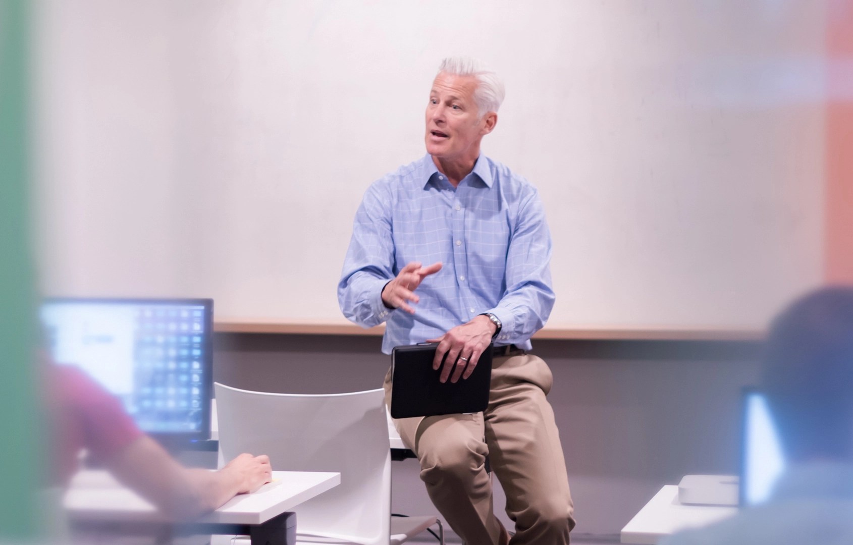 A GSTS trainer in a blue shirt sitting on a desk and engaging with participants during a classroom training session.