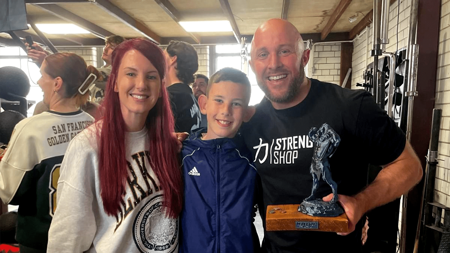 Kieren Stevens, GSTS Site Security Supervisor at Trafford General Hospital, holding a Strongman trophy with his wife and son