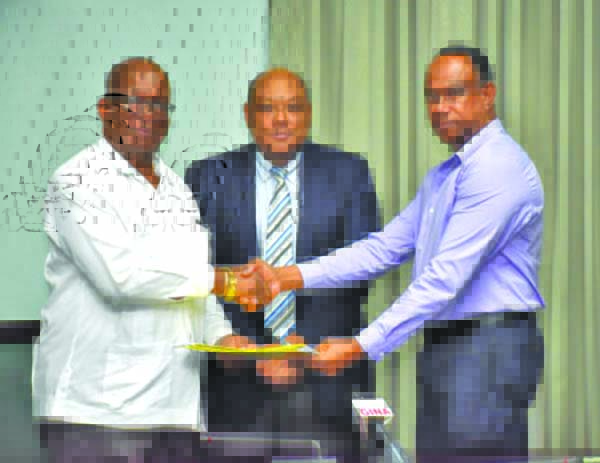 Finance Minister Winston Jordan and GGDMA President Terrence Adams shake hands after signing two agreements. Also in photo is Natural Resources Minister Raphael Trotman (centre)
