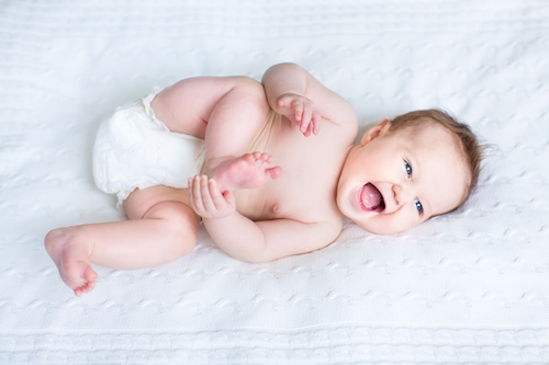 laughing baby in diaper playing with toes