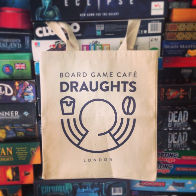 A tote bag with the Draughts café logo hangs in front of stacks of board games
