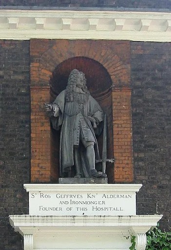 The metal statue of Sir Robert Geffrye in an alcove of red brick ontop of a white pedestal, embedded in a grey-brick wall