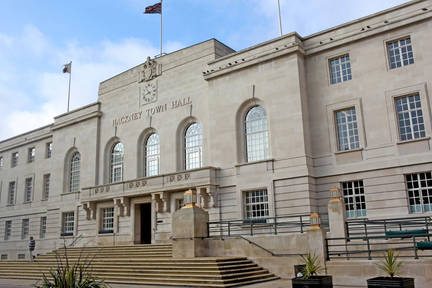 An image of Hackney Town Hall with a blue sky behind it. The grey stone building has steps leading up to it and many windows.