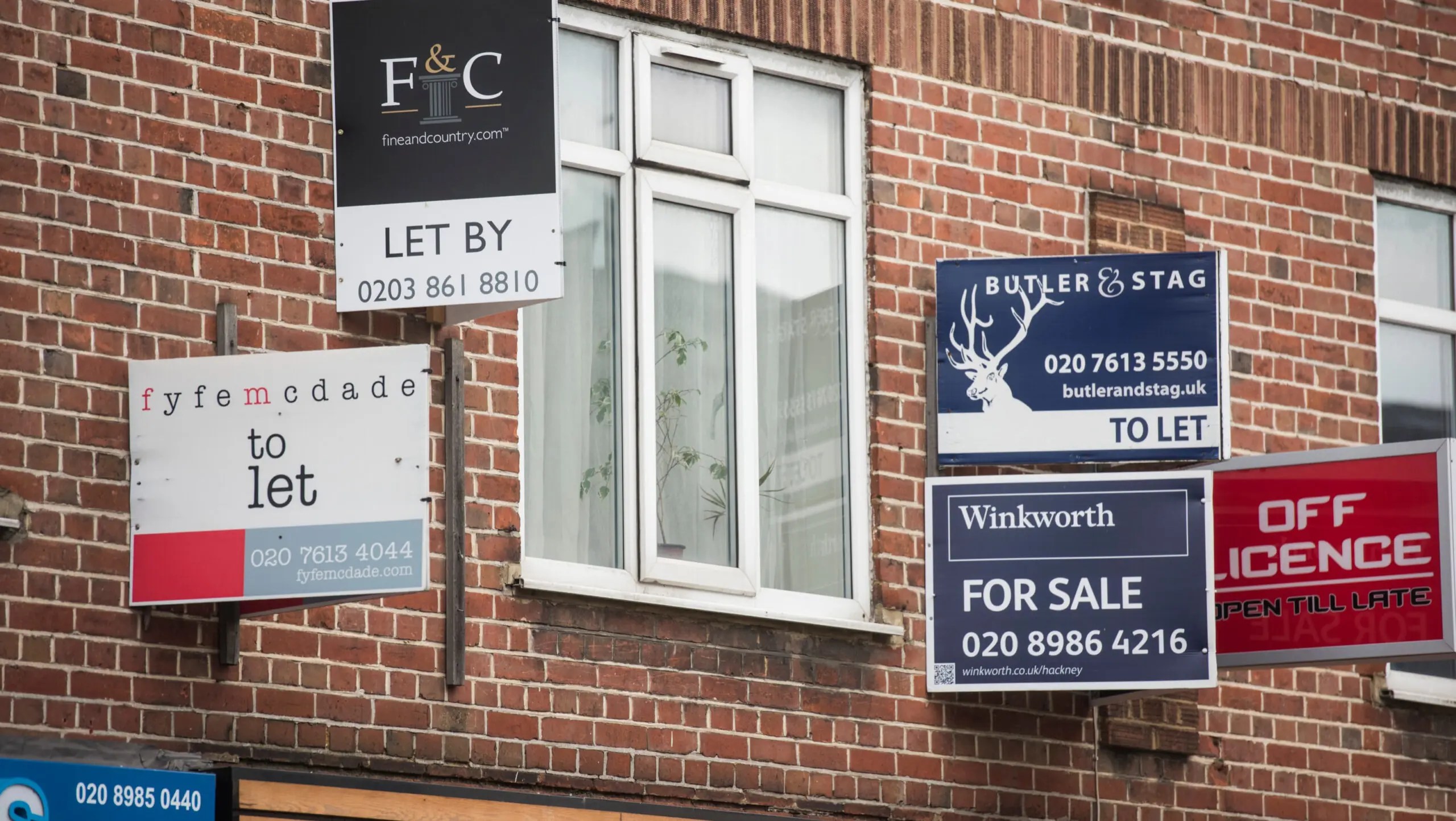 For sale and letting signs attached to a brick wall with a window in the centre.