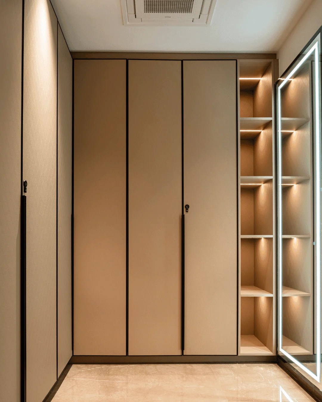 A premium walk-in closet space defined by a luxurious matte leather-finished wardrobe. This sophisticated unit includes seamless L-shaped leather panels, a sophisticated open display unit with integrated profile lighting, and a contemporary illuminated mirror, set on marble flooring.