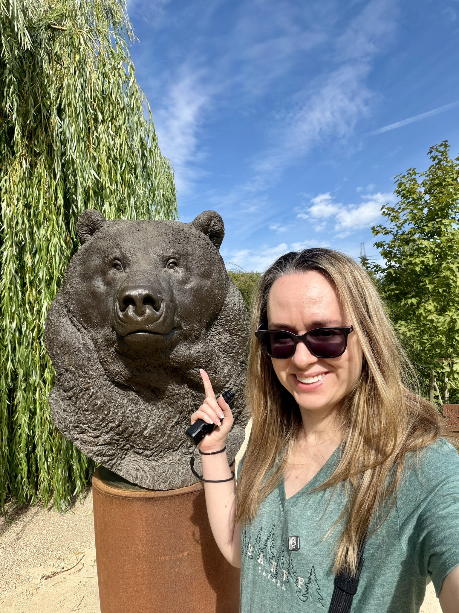 Lady in a green top stands in front of a bear sculpture while smiling and pointing at it.