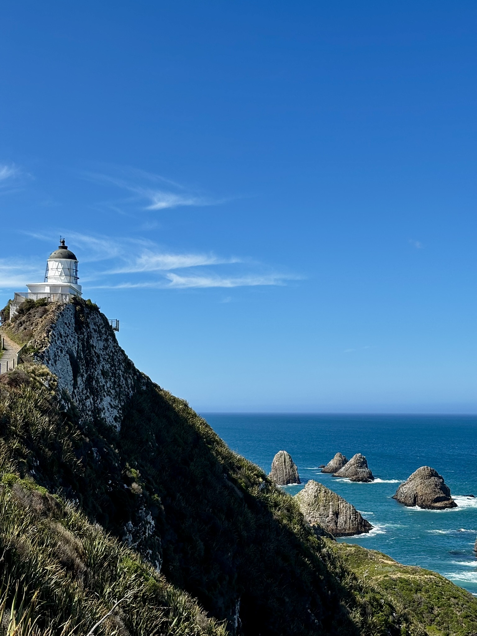Nugget Point Lighthouse above the rocky coastline and blue ocean in New Zealand