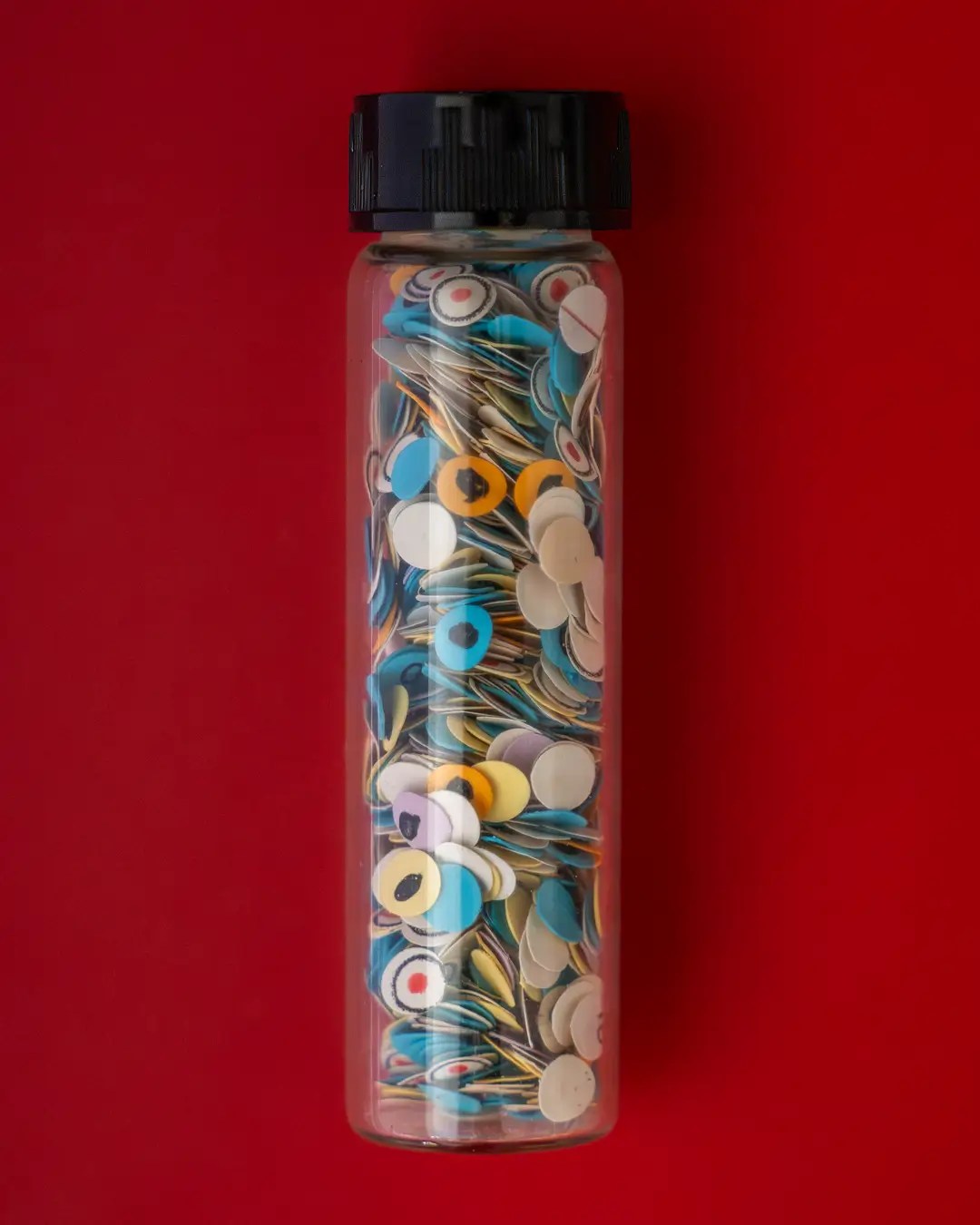 A close-up of a glass vial filled with small punched paper discs of many different colors. Each disc has some form of mark indicating where a test taker would have marked or filled in a circle as a test answer