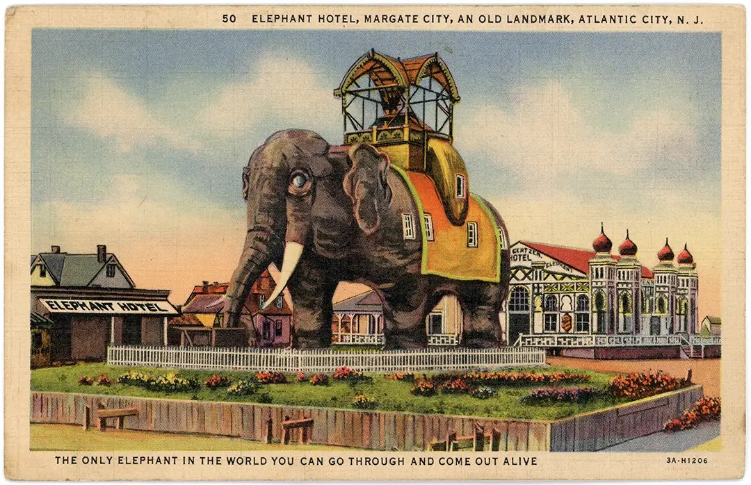 A vintage postcard front of the "Lucy the Elephant" building in in Margate City, New Jersey amid a landscaped park area with a white fence, flanked by small buildings and an ornate pavilion labeled "Elephant Hotel."