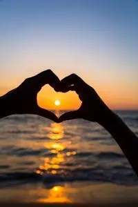 female hands in heart shape on sea beach at sunset background, Summer season