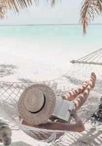 woman relaxing and reading while sitting in hammock on beach