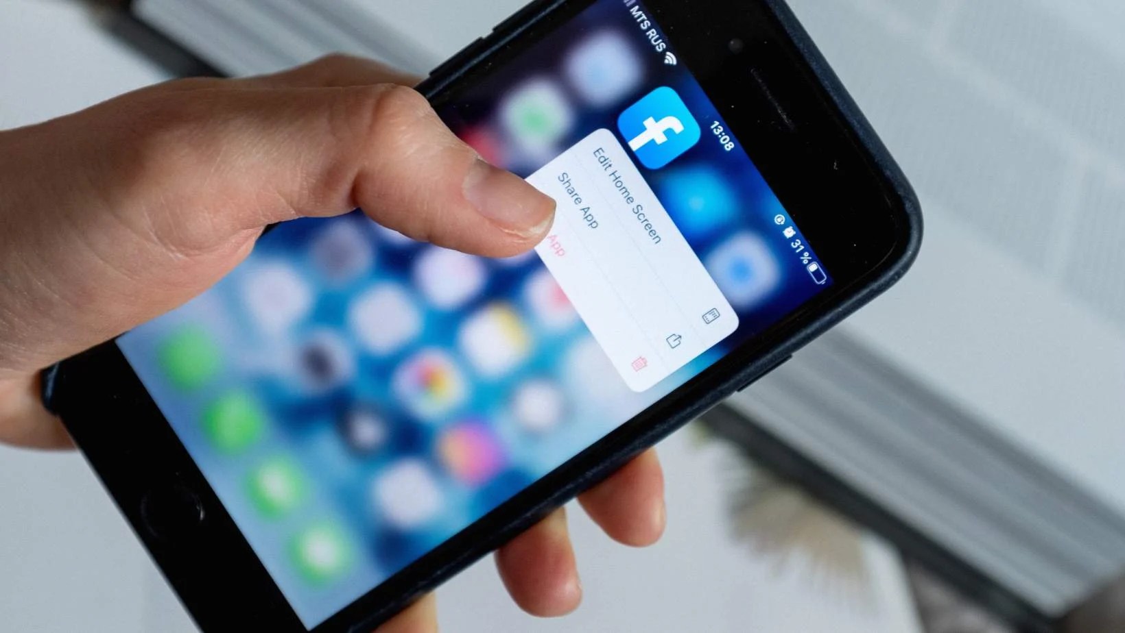 Person holding a phone, selecting the Facebook app.