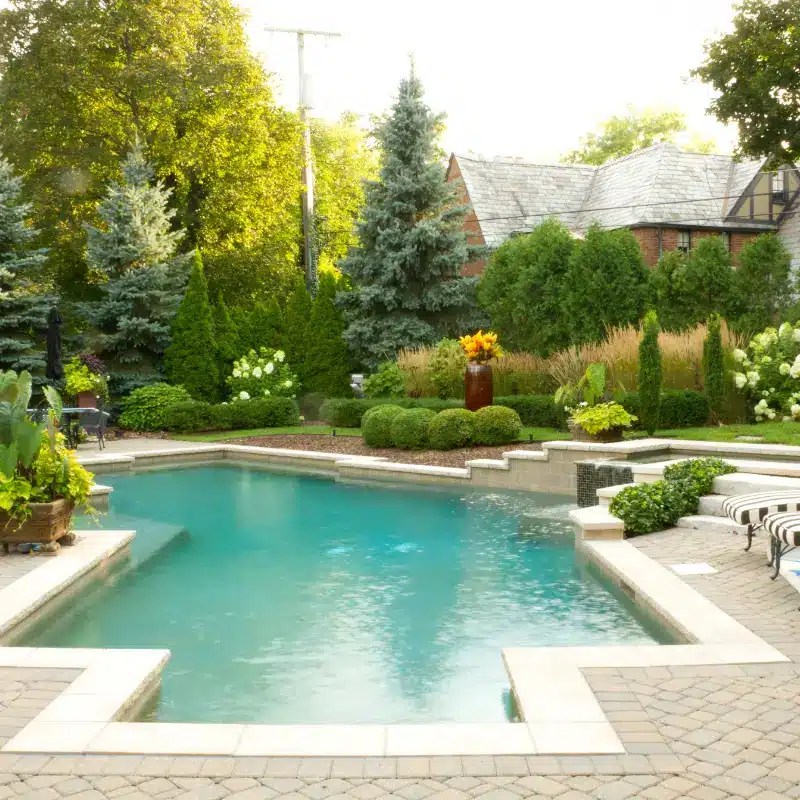 Close-up of a hand trimming hedges with a modern gardening tool, surrounded by lush greenery.