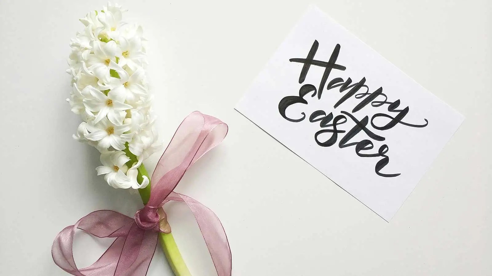 handwritten Happy Easter sign next two flowers tied with a bow