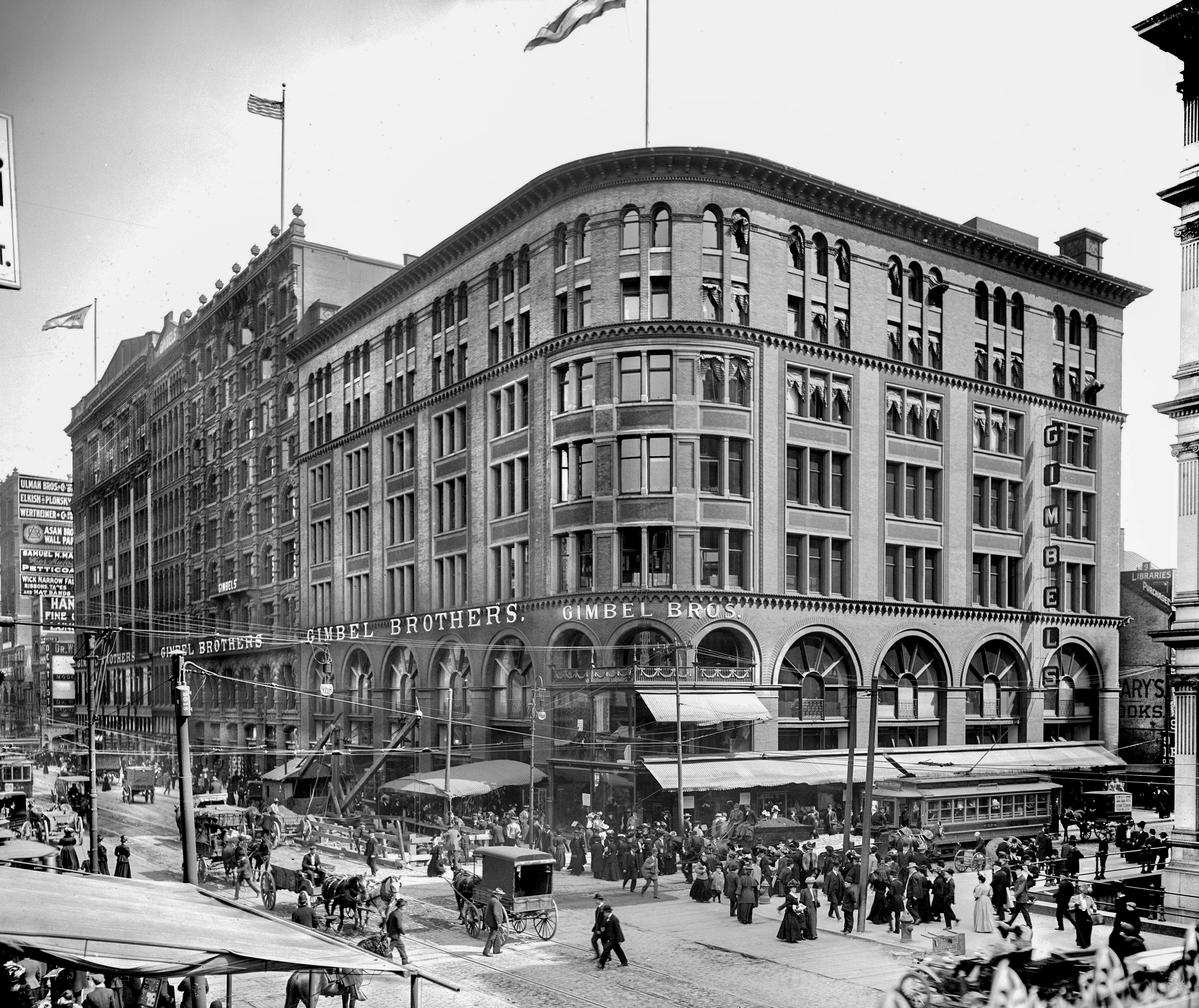 A 1920s black-and-white photo of a busy Philadelphia street with horse-drawn wagons, trolleys, and the Gimbel Brothers department store.