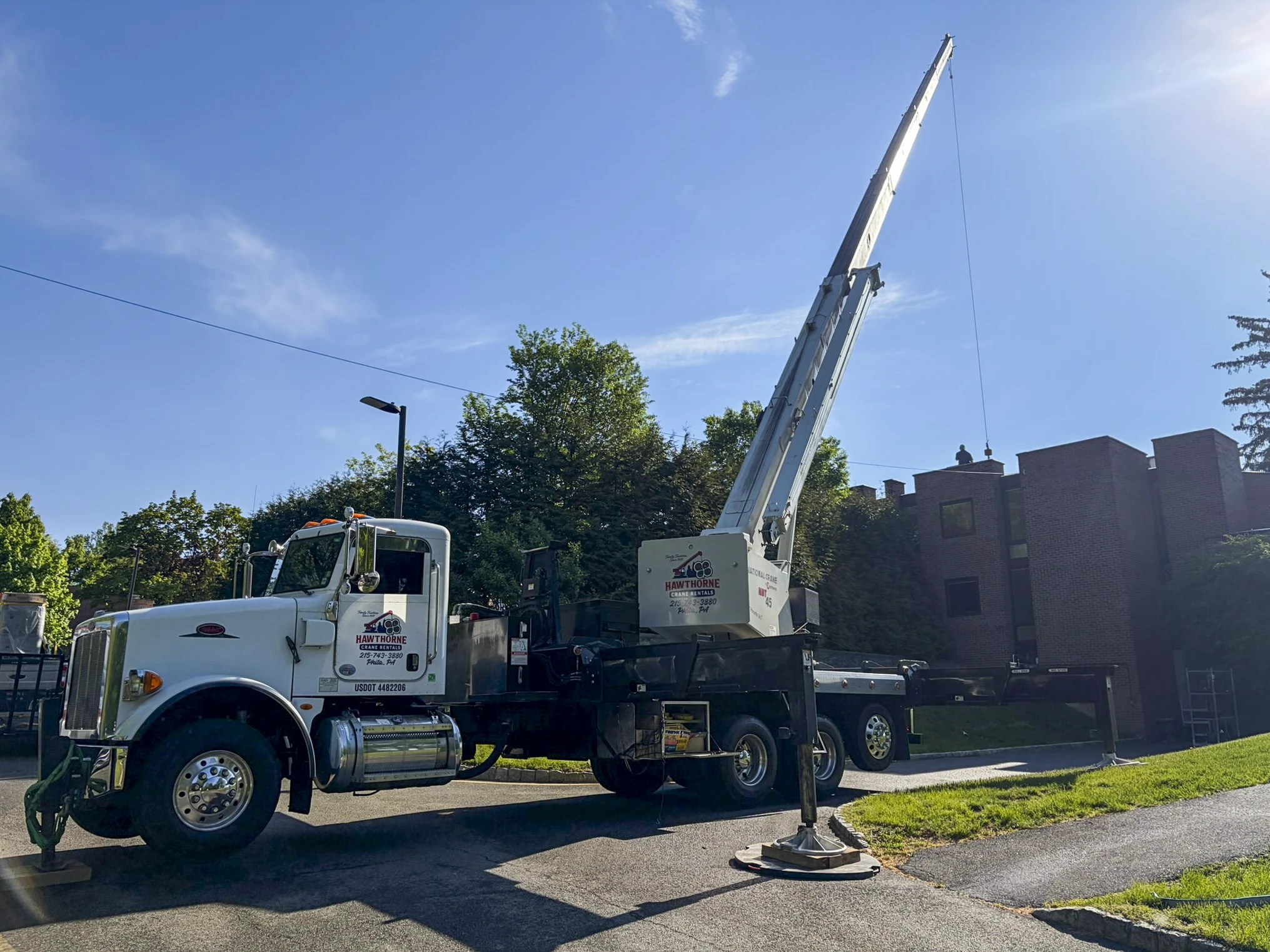 A Hawthorne National Crane NBT45 boom truck extends its crane to the rooftop of a multi-story brick building for a utility lift.