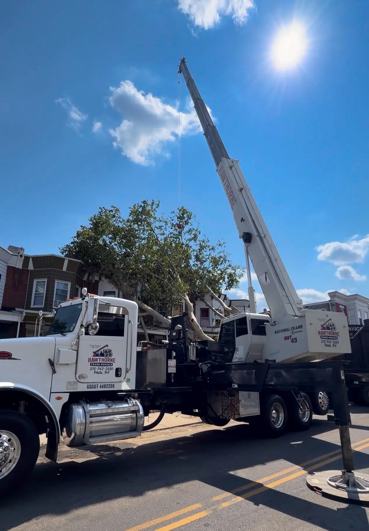 A Hawthorne Crane Rentals truck lifts a large fallen tree off the roof of a Philadelphia rowhome during an emergency response.