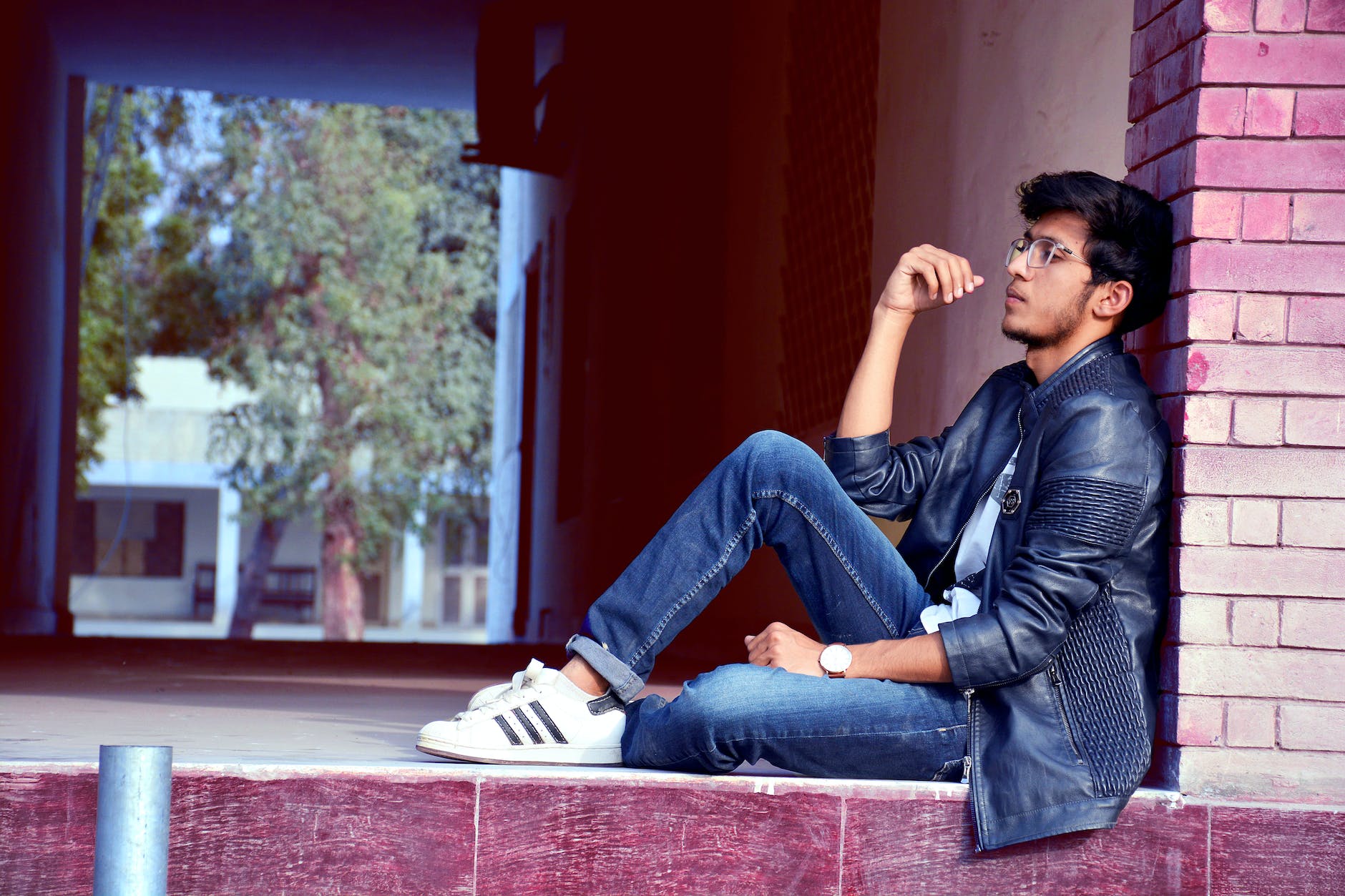 man wearing black leather jacket and blue jeans sitting on floor