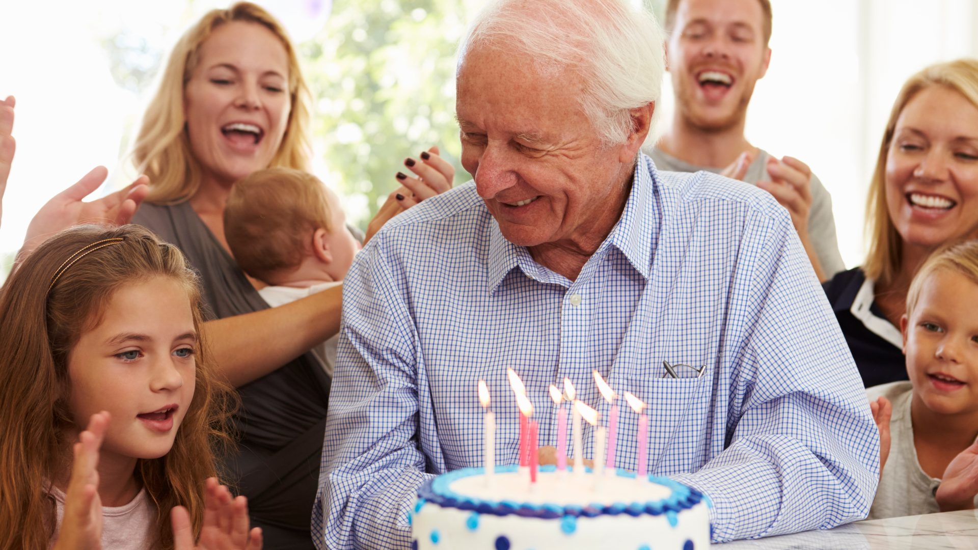 Grandfather Blows Out Birthday Cake Candles At Family Party