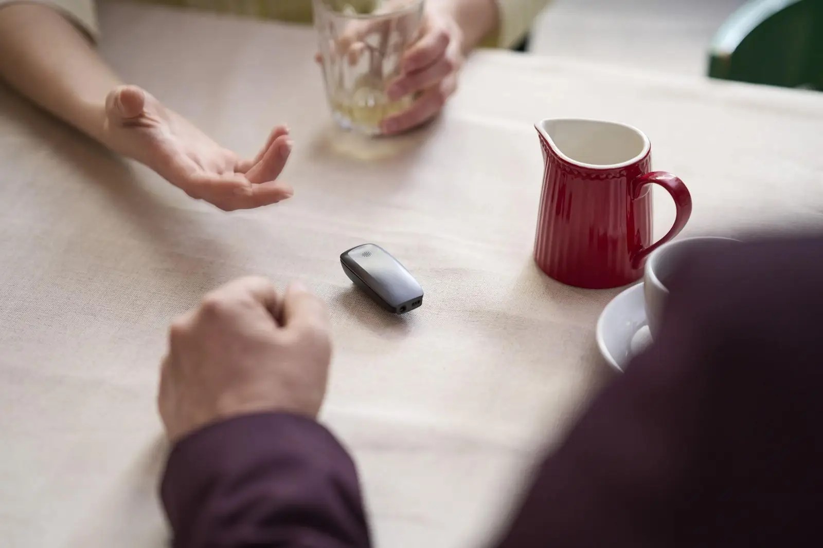 A ReSound Multi-Mic+ in the middle of a dining table with hands around it.
