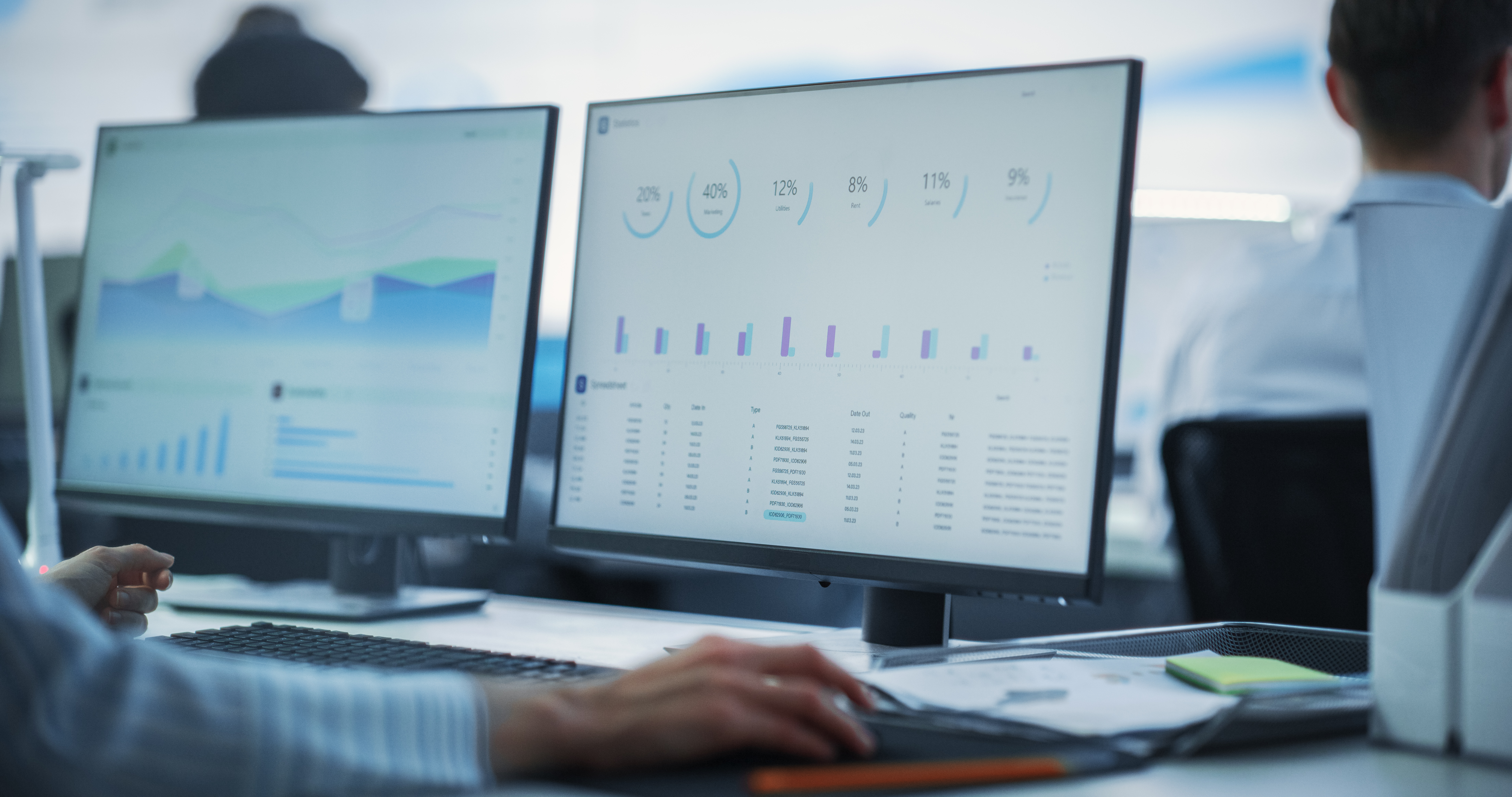 Person analyzing data on dual monitors displaying cybersecurity metrics and performance graphs in a modern office setting.