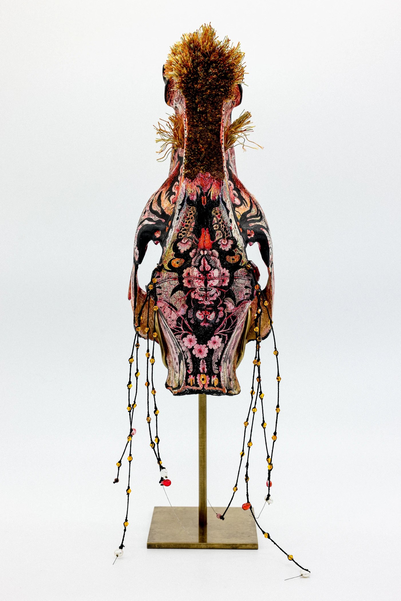 Crâne sculptural couvert de motifs roses et noirs, avec de longues parures de perles.