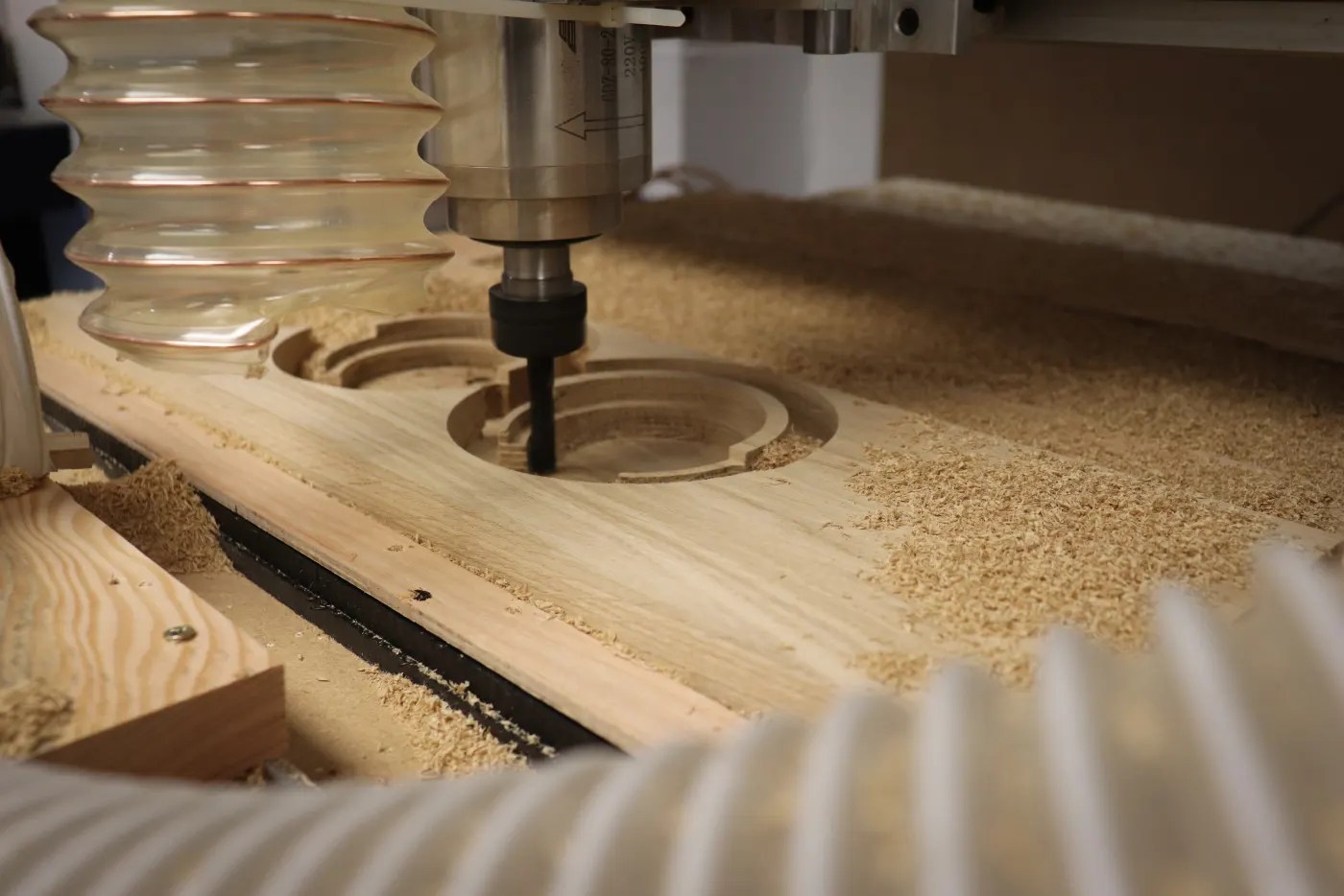 A CNC router cutting a circular recess into a timber blank, with sawdust around the cut