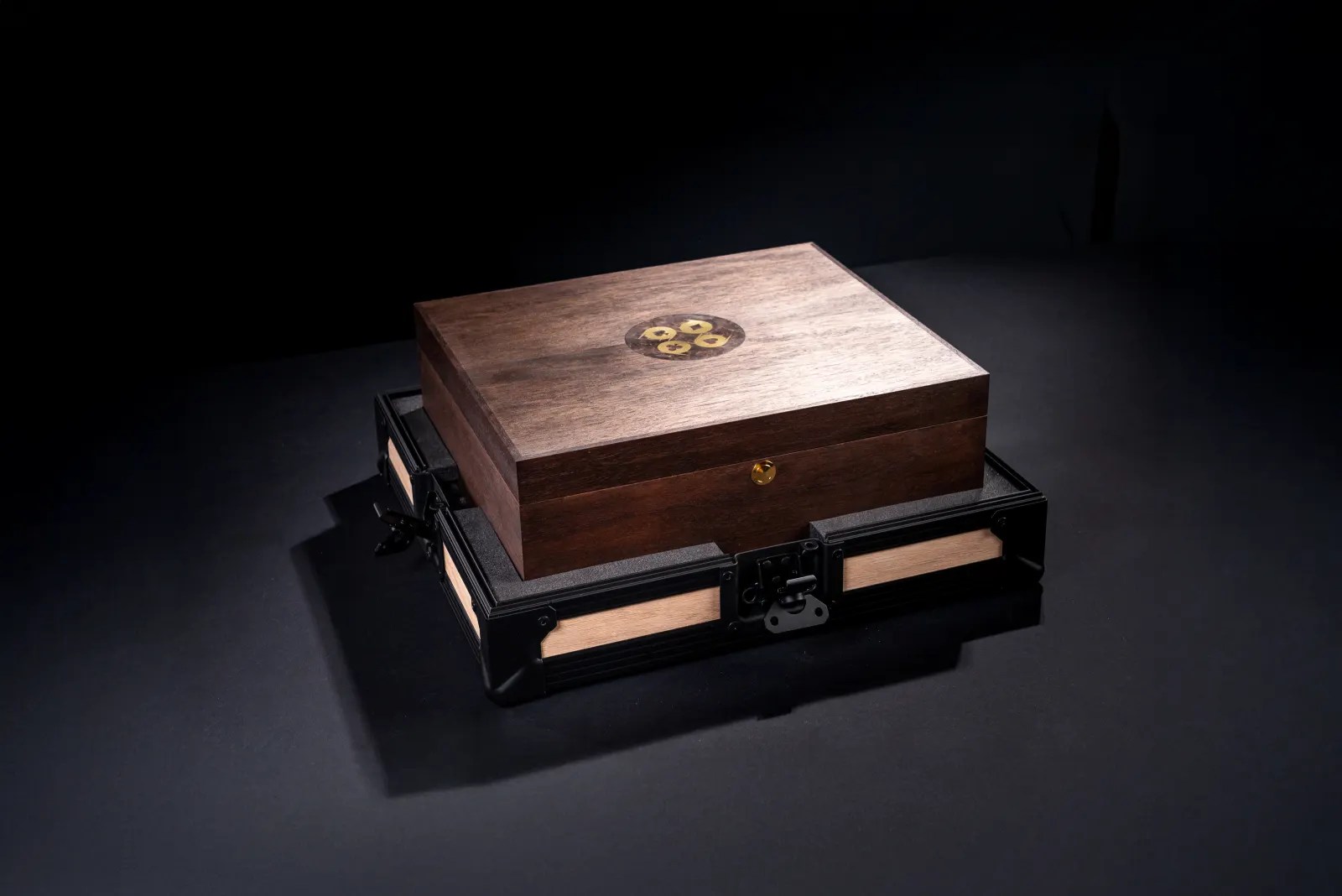 The closed walnut poker case with its inlaid logo on the lid, resting on a flight case