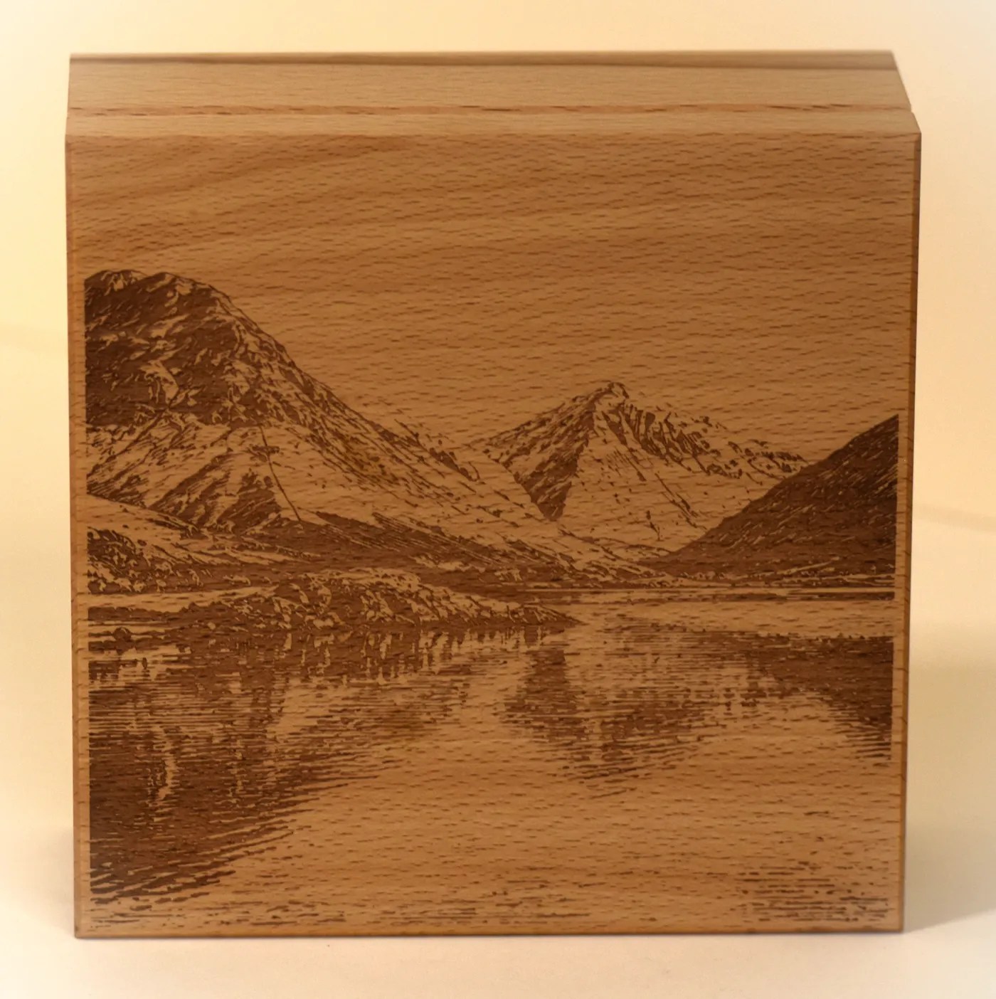 The lid of a beech box engraved with fells reflected in a still lake