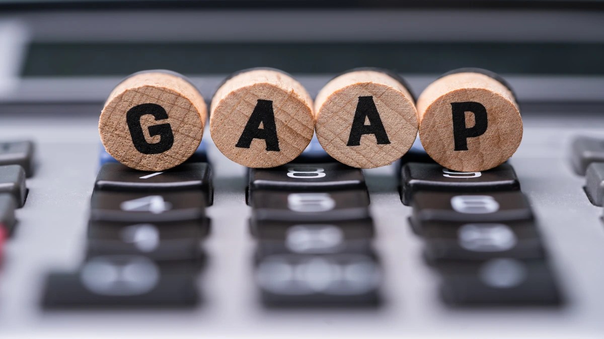 Four wooden blocks spelling out GAAP sitting on top of a calculator keyboard, representing revenue recognition standards under ASC 606 US GAAP.