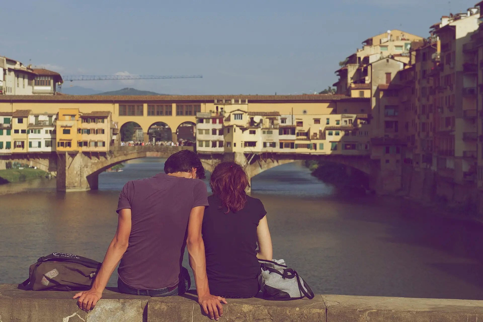 A couple sitting close together by a river, looking out at the view