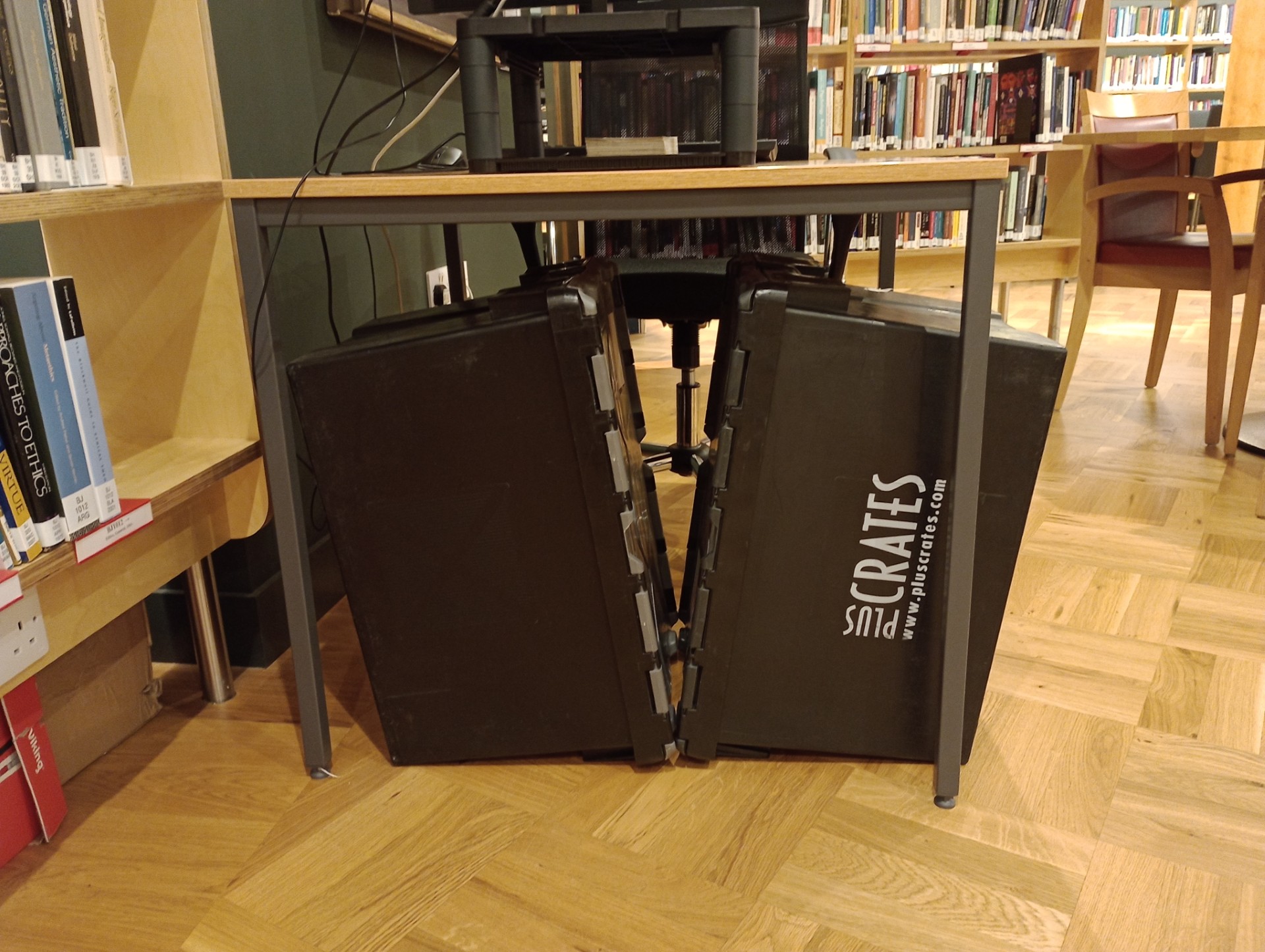 Two, black crates (used by Crown) sitting underneath a desk.