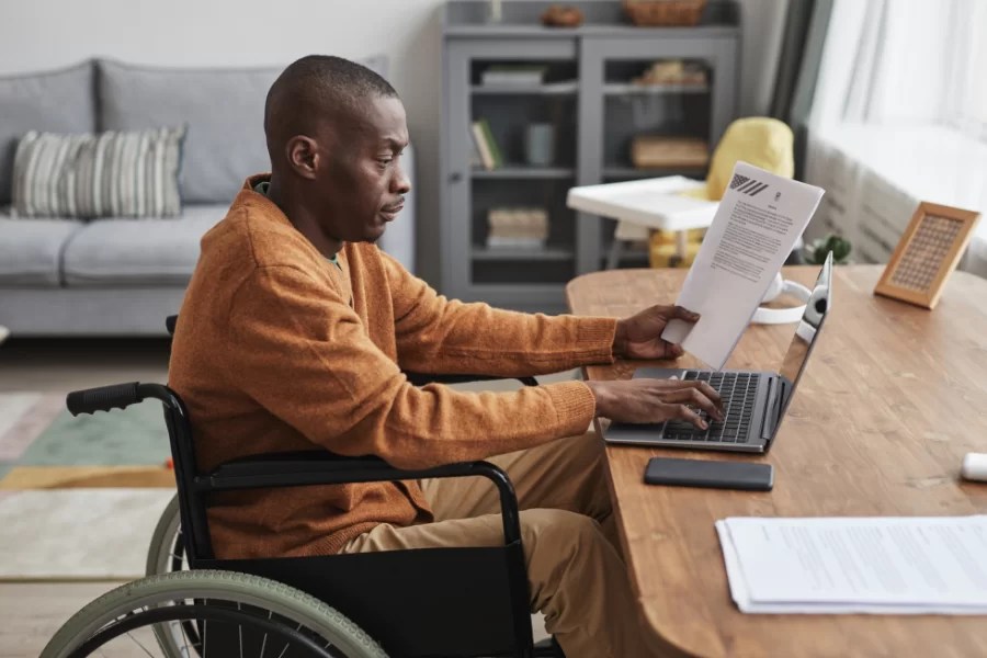 man in wheelchair working at a laptop on a desk