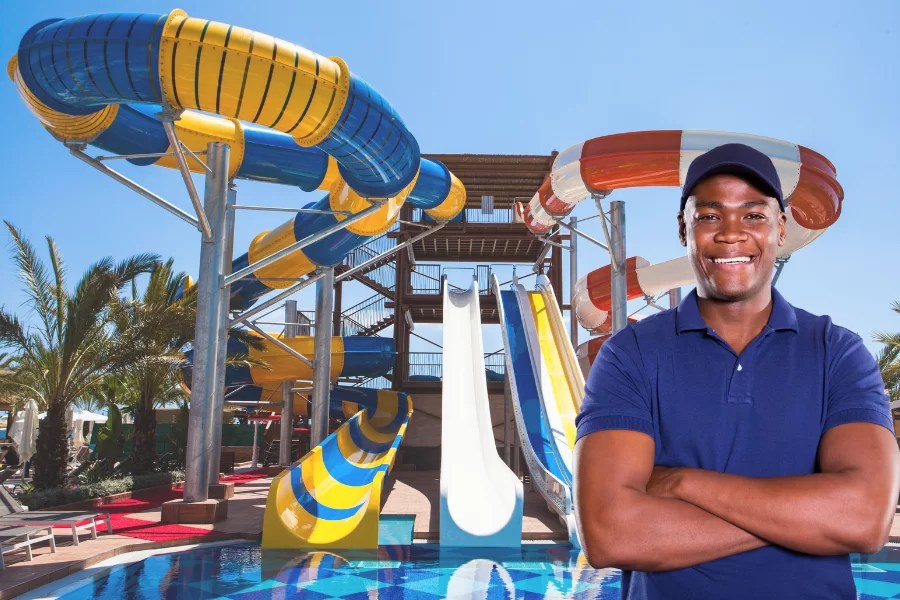 man stands happily in foreground with waterslides in background.