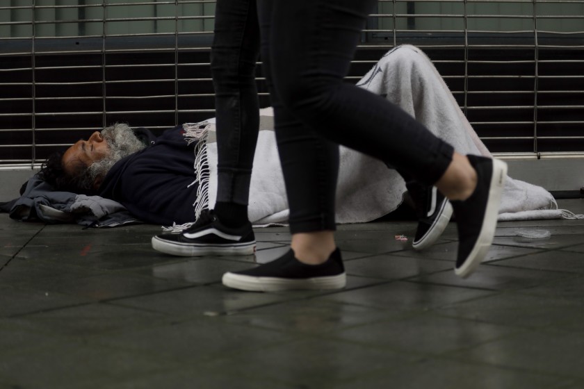 Covered with a blanket, a homeless person tries to stay warm as pedestrians walk past him in downtown Los Angeles.