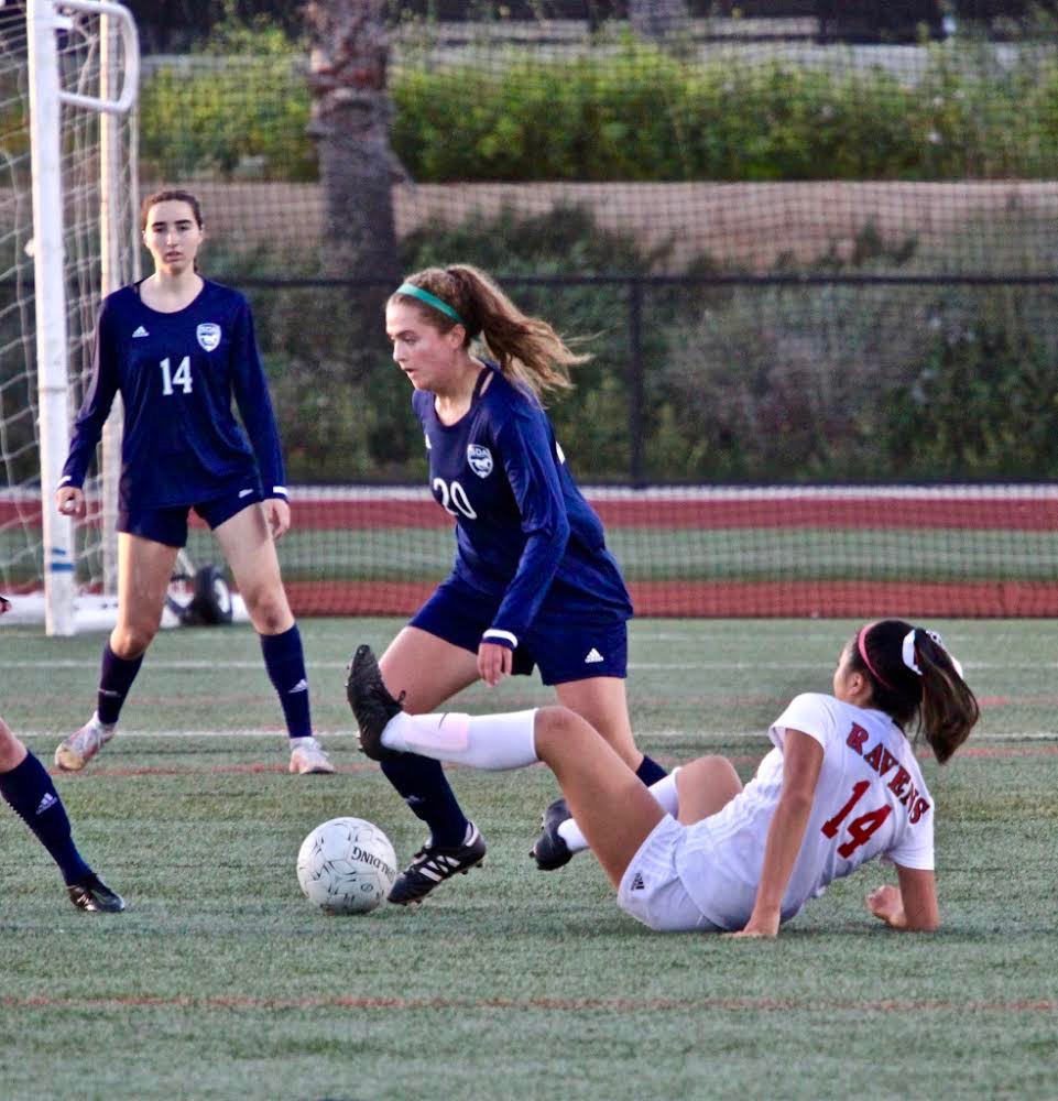 Bronwyn Eyre has the ball while two players are on the sidelines. One fell and one is standing up on the field.
