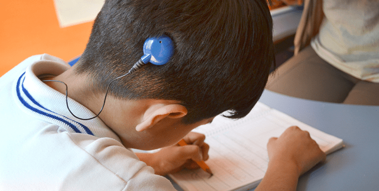 Fotografía de niño que usa un implante coclear. El niño se encuentra en la escuela haciendo tarea.