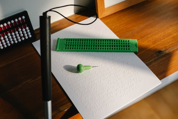 imagen de una hoja escrita en braille, un punzón, una regleta y un bastón