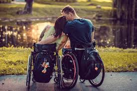 Imagen de dos personas usuarias de silla de ruedas, dándose un abrazo, están dando la espalda a la foto