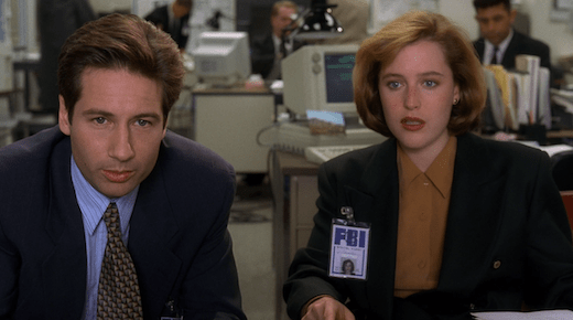 Mulder and Scully lean in to view evidence.