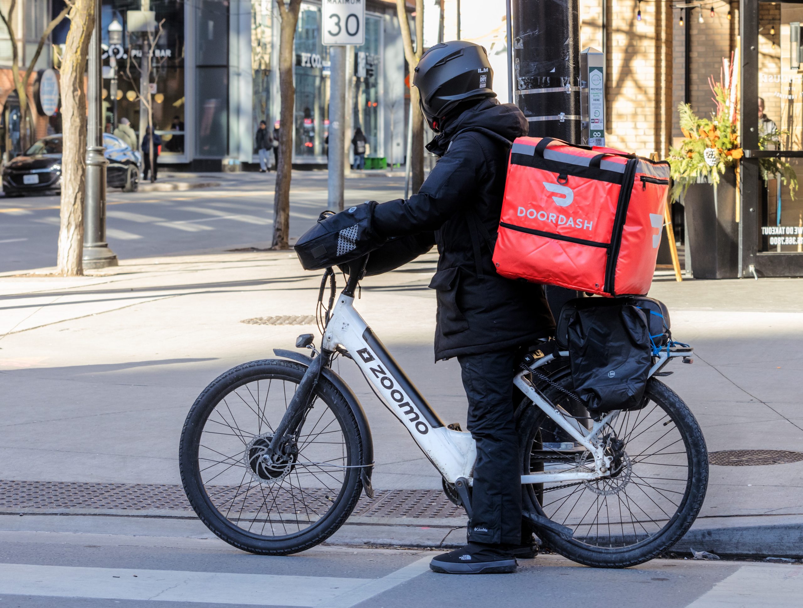A DoorDash food delivery courier on an electric bicycle, or e-bike, with the distinctive red back pack on a downtown street in Atlanta, GA