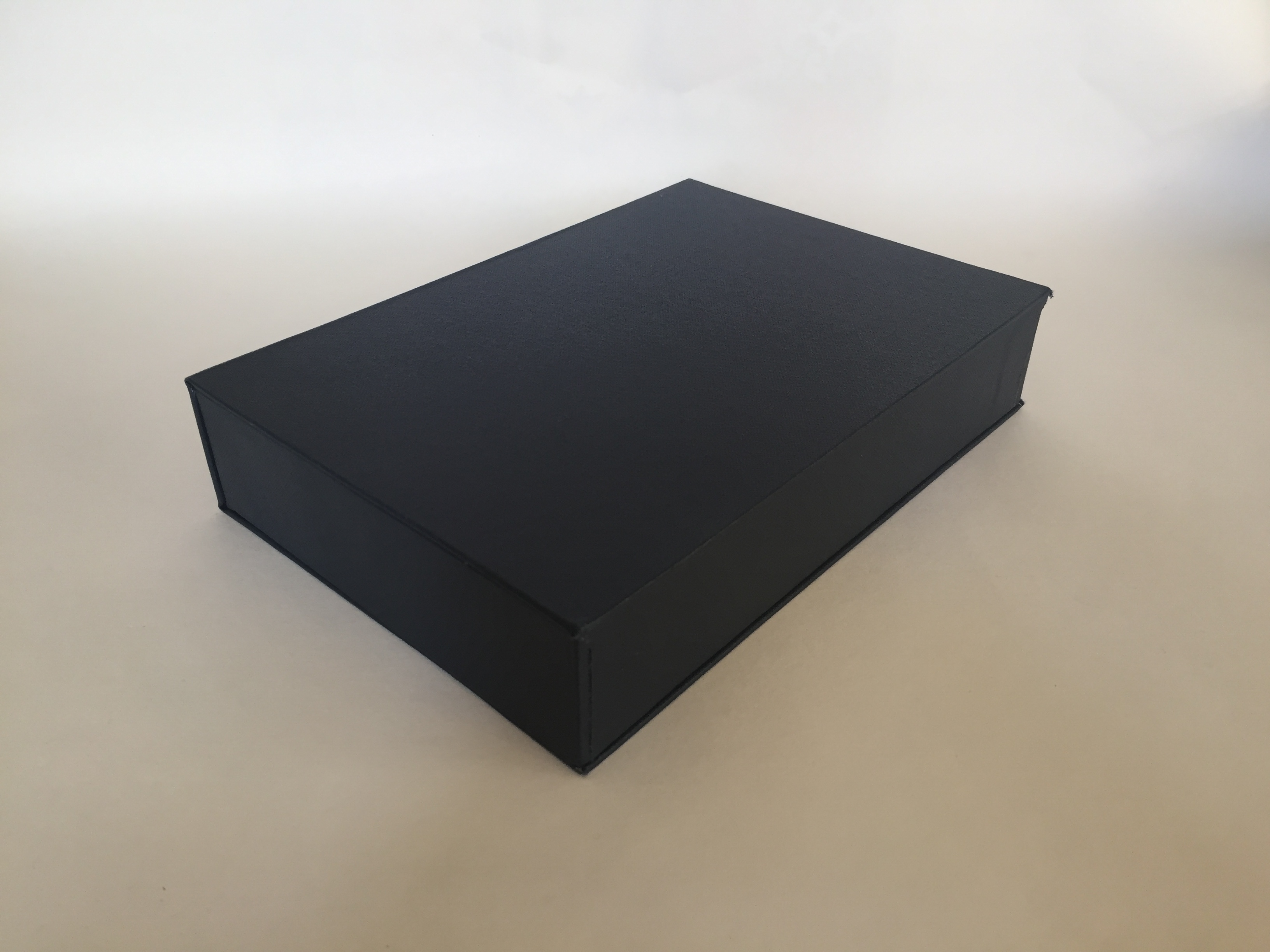 Image of a clamshell or drop spine box made from millboard and covered in blue bookcloth closed flat on a surface