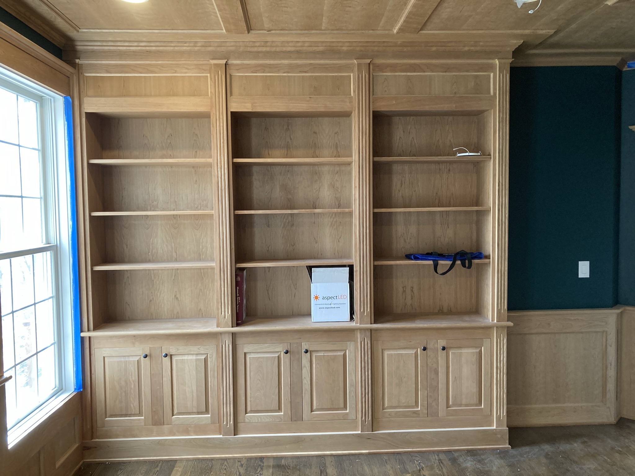 Custom floor-to-ceiling built-in bookcases for a home office, featuring natural wood cabinetry, open shelving, lower cabinet storage, detailed trim, and crown molding.